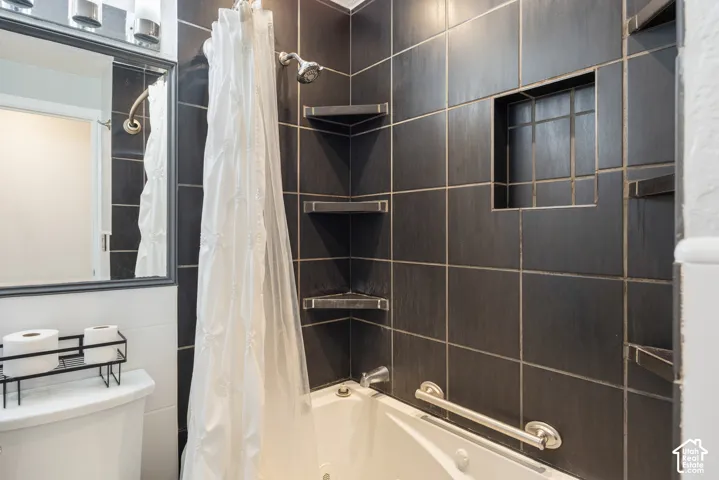 Tiled shower and bath combination with a built-in niche, integrated corner shelving, and a polished chrome grab bar