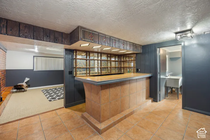 Built-in bar with tile finish and integrated shelving, overhead lighting, and wood-finish cabinetry