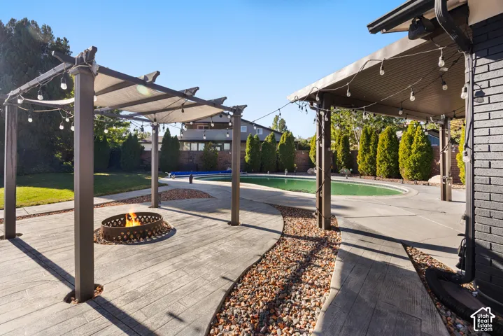 Expansive backyard featuring a covered patio, an additional pergola with a fire pit, a curved concrete pathway, and a swimming pool
