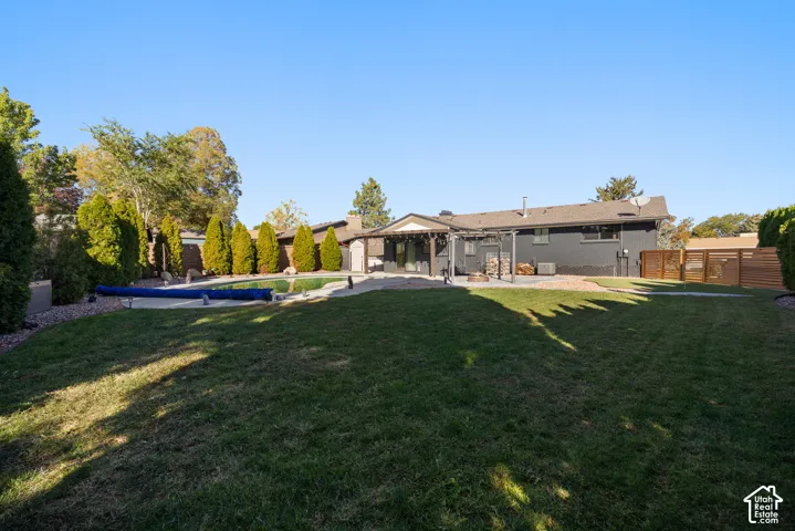 Expansive backyard featuring a lush lawn, mature trees, a swimming pool with a cover, a paved patio, and a covered pergola
