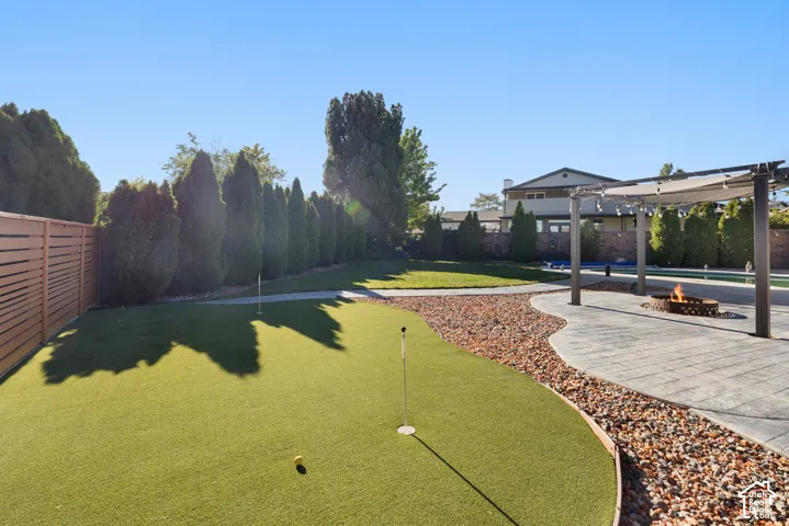 Expansive backyard oasis featuring a manicured synthetic putting green with integrated golf hole, decorative river rock landscaping, mature privacy hedging along perimeter, and adjoining composite decking with pergola structure