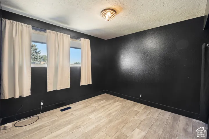 Spacious room featuring dramatic black accent walls, wood-finish flooring, and large windows with cream curtains allowing abundant natural light