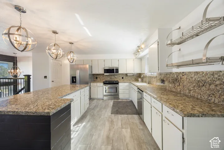 Chef's kitchen featuring white cabinetry, stainless steel appliances, dual granite countertops with waterfall island edge, wood-finish flooring, and pendant lighting