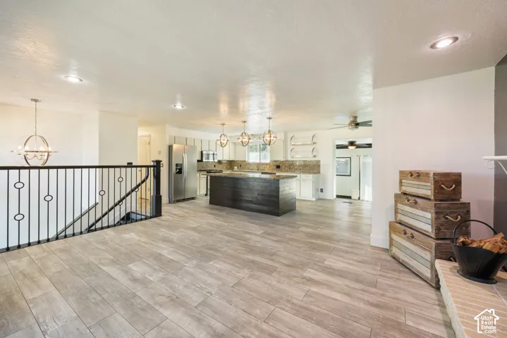 Open-concept living space with wood-finish flooring, a kitchen island, stainless steel appliances, and an open railing staircase