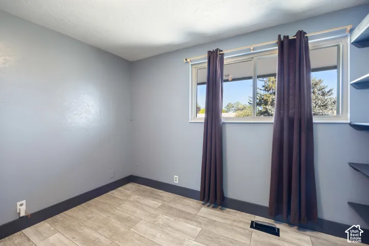 Bright bedroom featuring large dual windows with natural light, wood-finish flooring throughout, fresh paint in soft blue tones, and dark purple thermal curtains