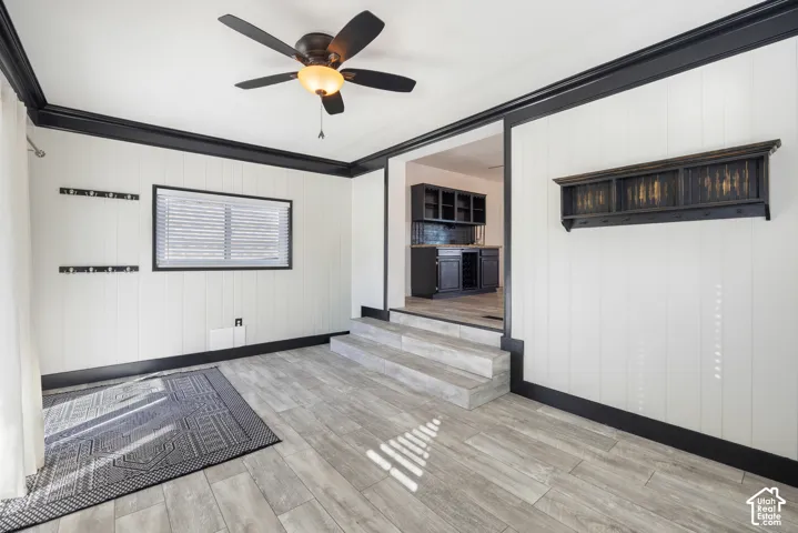 Wood-finish plank flooring, paneled walls with black trim, and a ceiling fan with integrated lighting