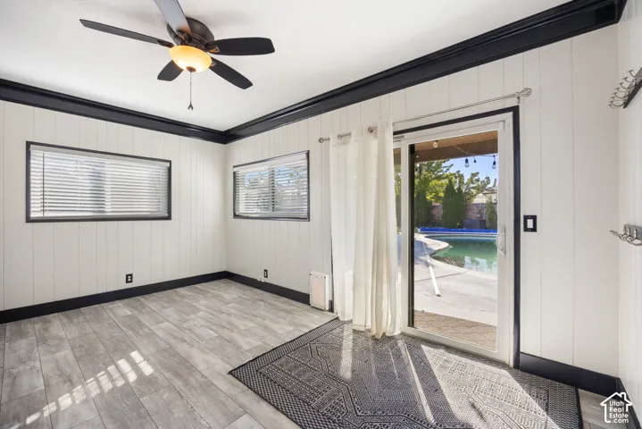 Wood-finish flooring, two windows with blinds, built-in ceiling fan with light fixture, sliding glass door, and backyard pool with concrete surround