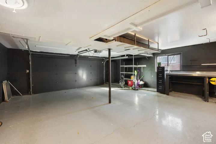 Spacious garage featuring polished concrete flooring, overhead storage systems, black finished walls, and abundant natural light from clerestory windows and entry door