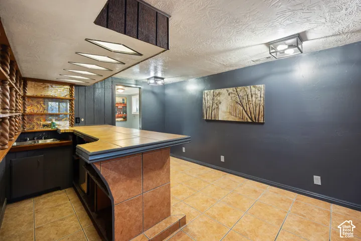Built-in bar with a tile countertop, integrated sink, and cabinet storage