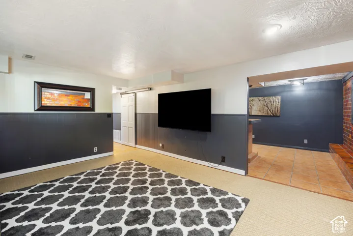 Finished basement recreation room featuring two-tone painted walls with charcoal lower half, recessed ceiling lighting, wall-mounted flat-screen television, wood-finish flooring, and geometric patterned area rug