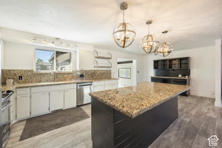 Kitchen featuring a large central island with a granite countertop, coordinating granite backsplash, white cabinetry, wood-finish flooring, and three spherical pendant lights