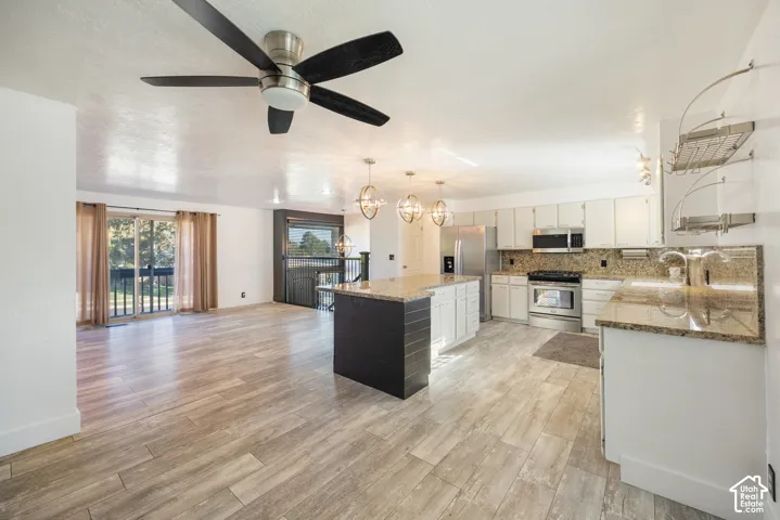 Open-concept living space featuring wood-finish flooring, a kitchen island with granite countertops, stainless steel appliances, and a sliding glass door leading to an outdoor area