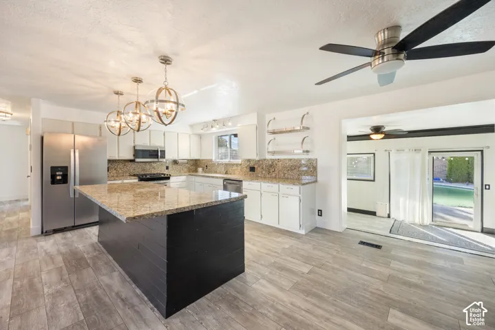 Kitchen featuring wood-finish flooring, a central island with a stone countertop, stainless steel appliances, white cabinetry, and recessed lighting