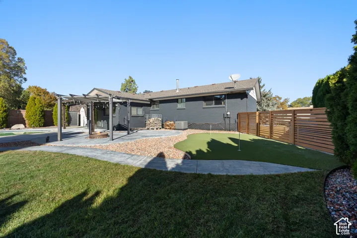 Expansive backyard featuring a pergola-covered patio, fire pit, putting green, and wood privacy fencing