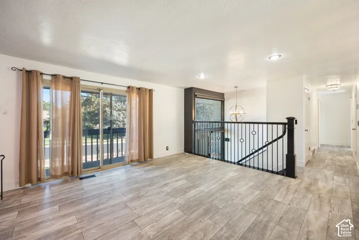 Spacious open-concept loft featuring wide-plank wood-finish flooring, floor-to-ceiling glass doors with sheer drapery panels opening to a private balcony, recessed ceiling lighting, and a black metal stair railing with modern spindle design
