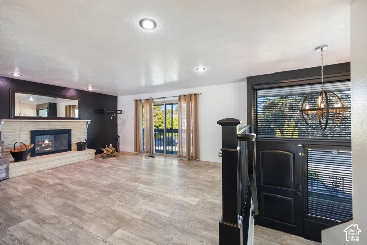 Spacious living area featuring wood-finish flooring, a gas fireplace with custom surround and mirror detailing, recessed ceiling lighting, and sliding glass doors with louvered window treatments