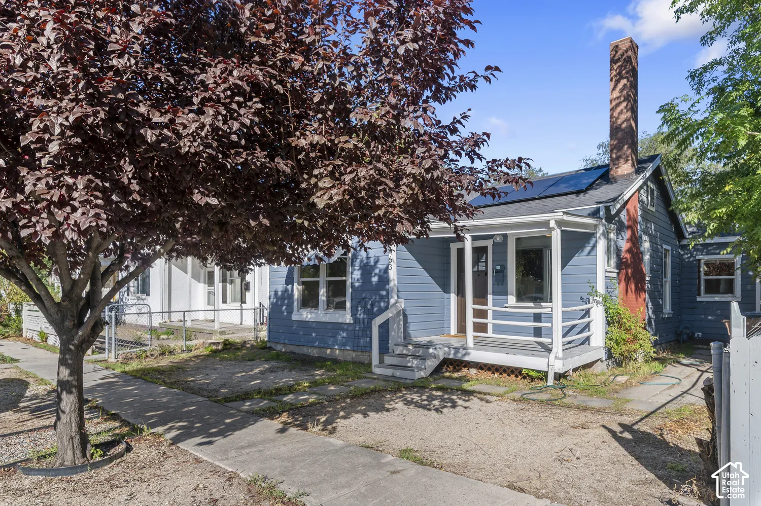 Exterior featuring blue siding, white trim, a covered porch, and a prominent brick chimney