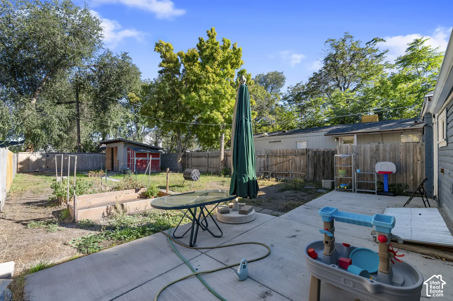 Concrete patio with a wood privacy fence, raised garden beds, and a storage shed