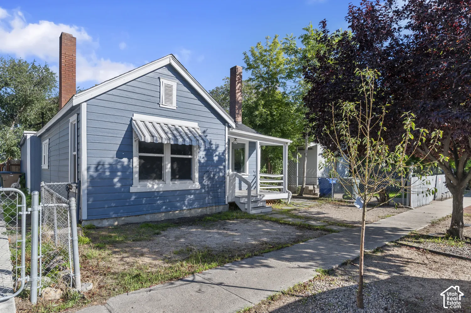 Blue siding exterior with white trim, featuring a front porch with white railings and an awning over the front window