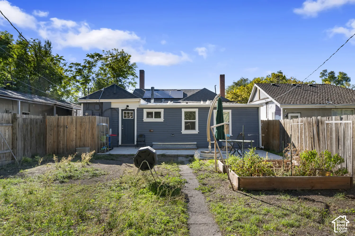 Rear exterior with a concrete patio, wood fencing, and raised garden beds