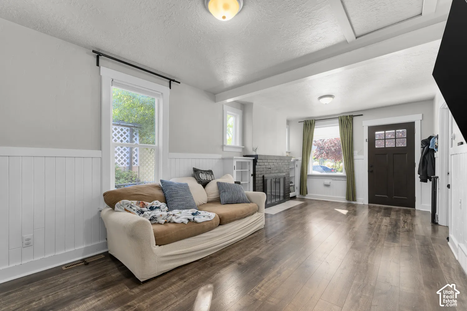 Expansive living area featuring wood-finish flooring, white wainscoting, and exposed ceiling beams
