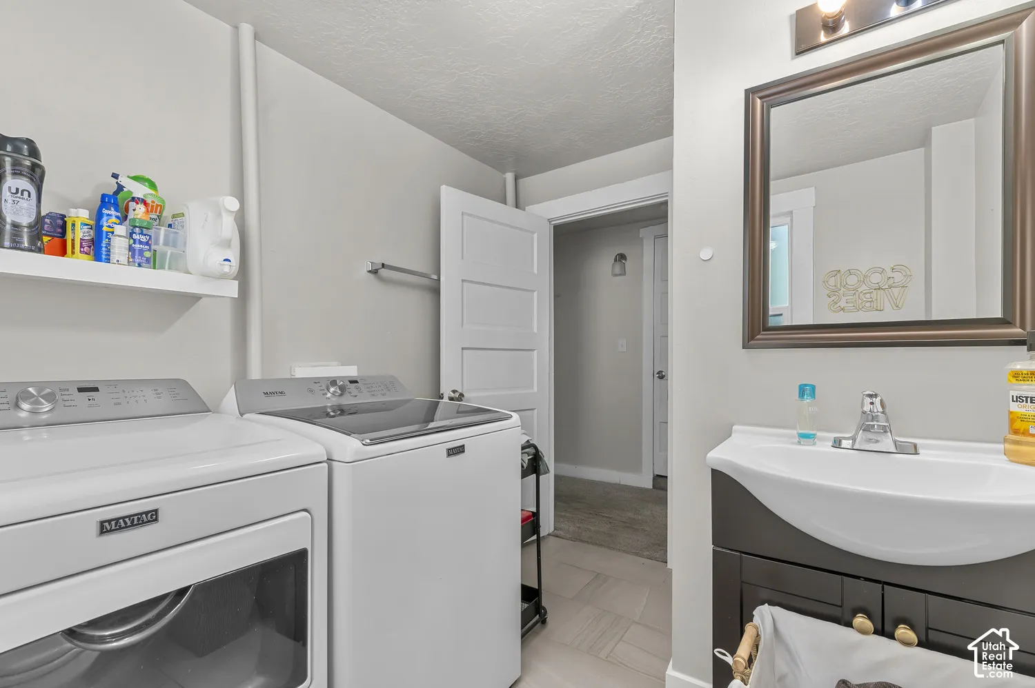 Integrated laundry appliances, wall-mounted shelving, contemporary vanity with an integrated sink, framed wall mirror, and modern lighting fixture