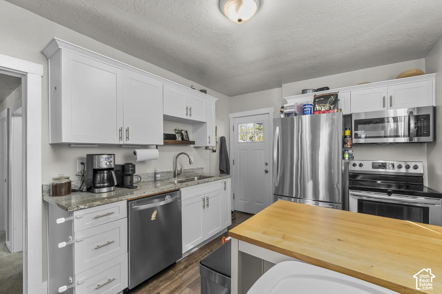 Kitchen featuring white cabinetry, granite countertops, stainless steel appliances, and wood-finish flooring
