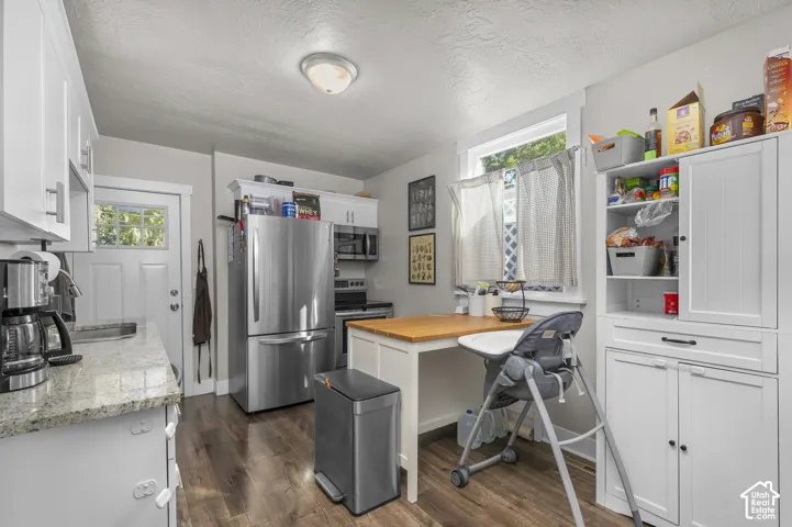 Wood-finish flooring, white cabinetry with silver-tone hardware, granite-style countertops, stainless steel appliances, and a built-in kitchen island with a wood-finish top