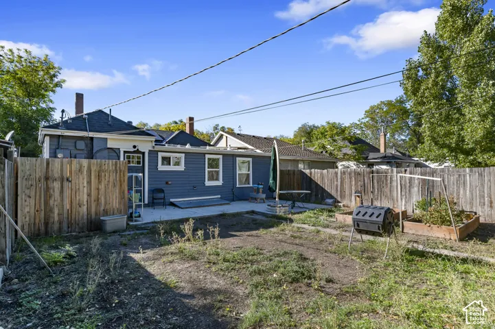 Rear exterior with blue horizontal siding, white trim windows, concrete patio, and fenced perimeter