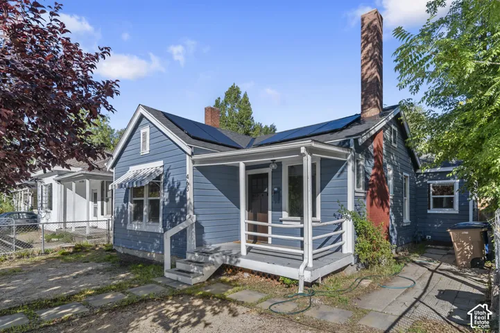 Blue clapboard exterior with white trim, covered front porch, an awning over a front window, a brick chimney, and rooftop solar panels