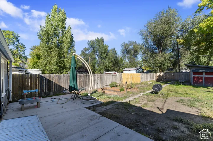 Expansive backyard with a concrete patio, wood privacy fencing, a raised garden bed, and mature trees