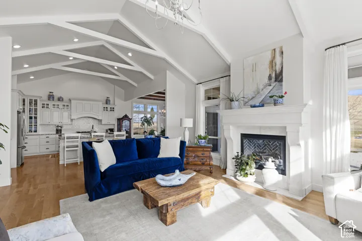 Open-concept living area featuring soaring vaulted ceilings with exposed beam detailing, a wood-finish floor throughout, and abundant natural light from multiple windows