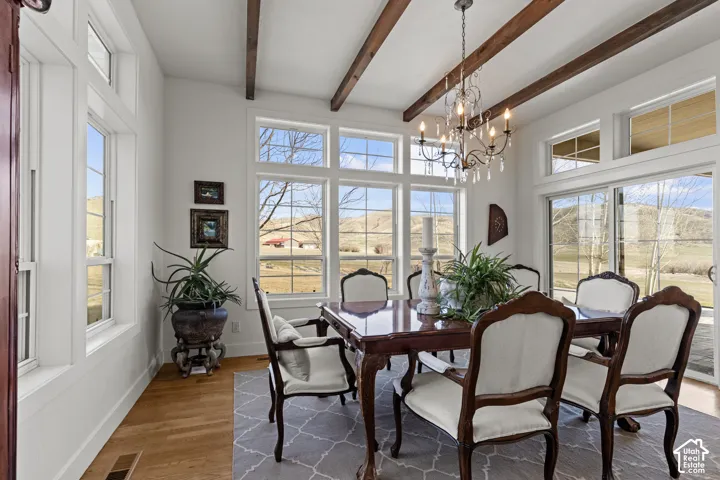 Exposed ceiling beams, abundant natural light, wood-finish flooring, sliding glass door, and a crystal chandelier