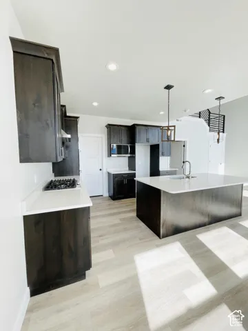 Kitchen featuring dark wood-finish cabinetry, white countertops, a gas range, a large central island with an undermount sink, and wood-finish flooring