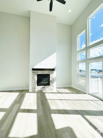 Two-story ceilings, ceiling fan, wood-finish flooring, stone-clad fireplace with mantel, and large windows