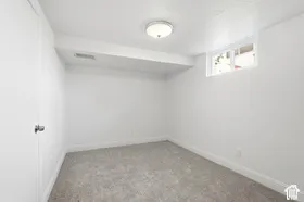 Carpeted flooring, white painted walls, recessed window, flush mount ceiling light, and a white door with a silver knob