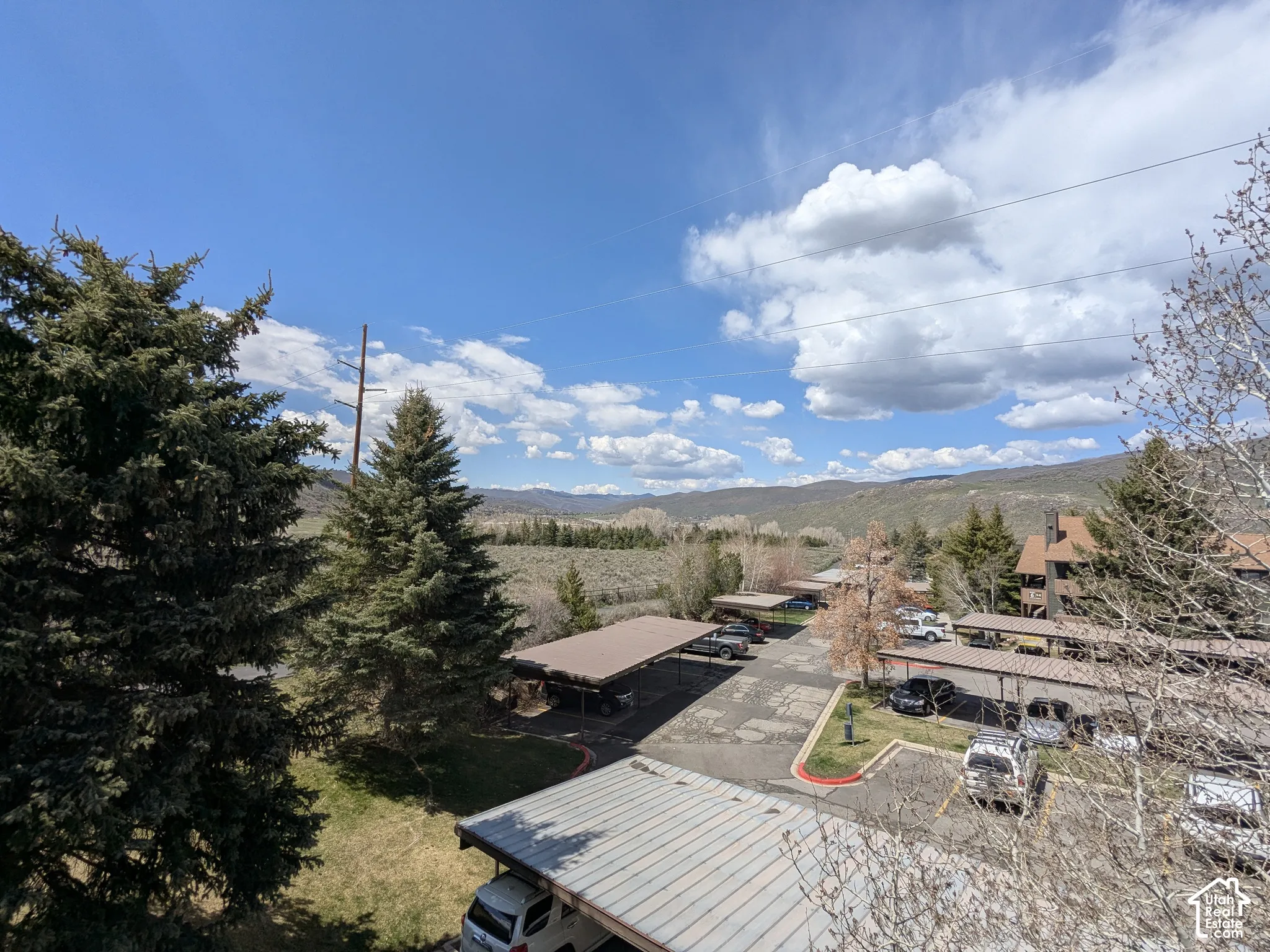 Expansive mountain landscape with mature evergreen trees, multiple covered parking structures, and a multi-level building featuring a brown exterior and pitched roofs