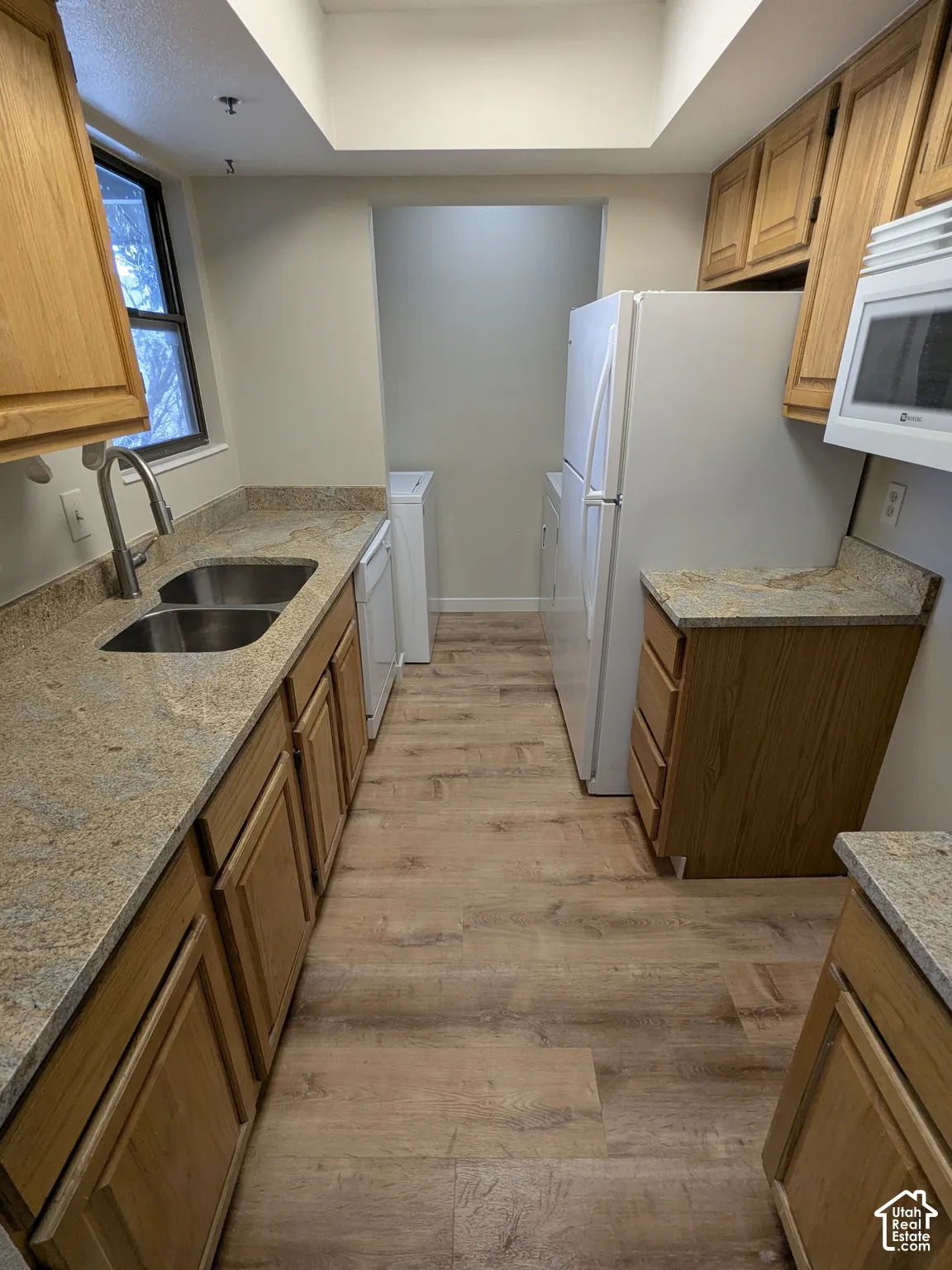 Galley kitchen featuring wood-finish flooring, wood cabinetry, stone countertops, and a double basin sink