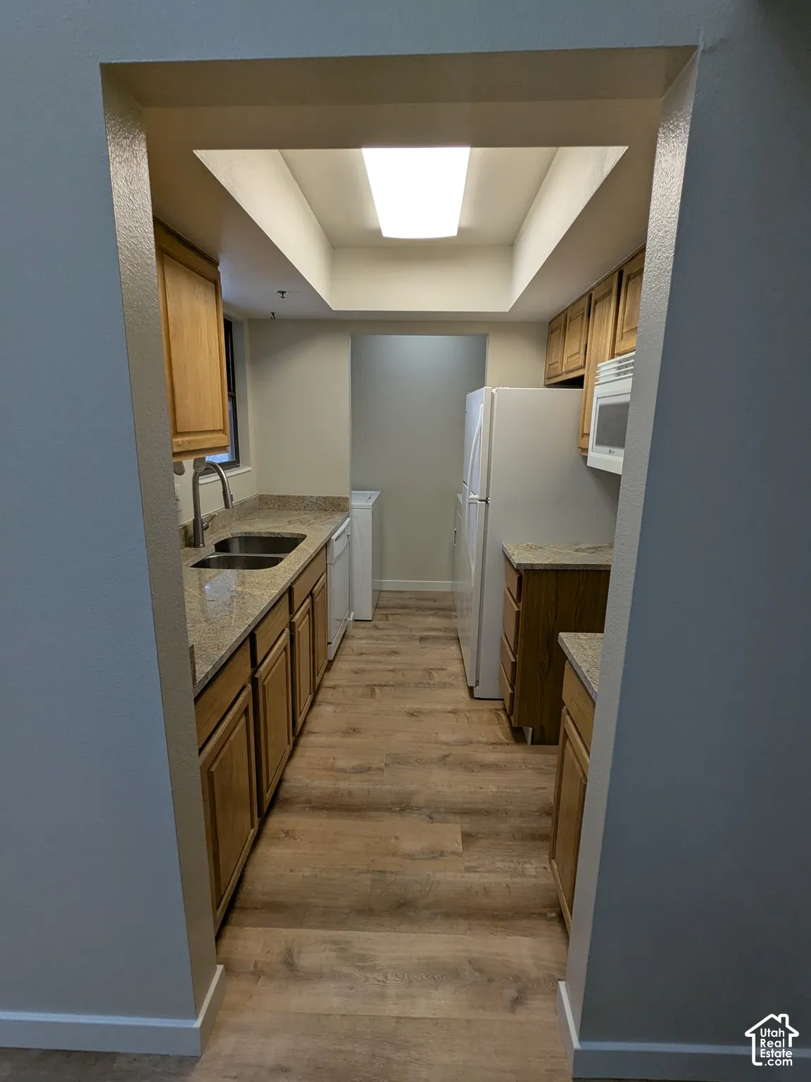 Galley kitchen featuring wood-finish flooring, wood cabinetry, stone-look countertops, a stainless steel sink, and a built-in microwave