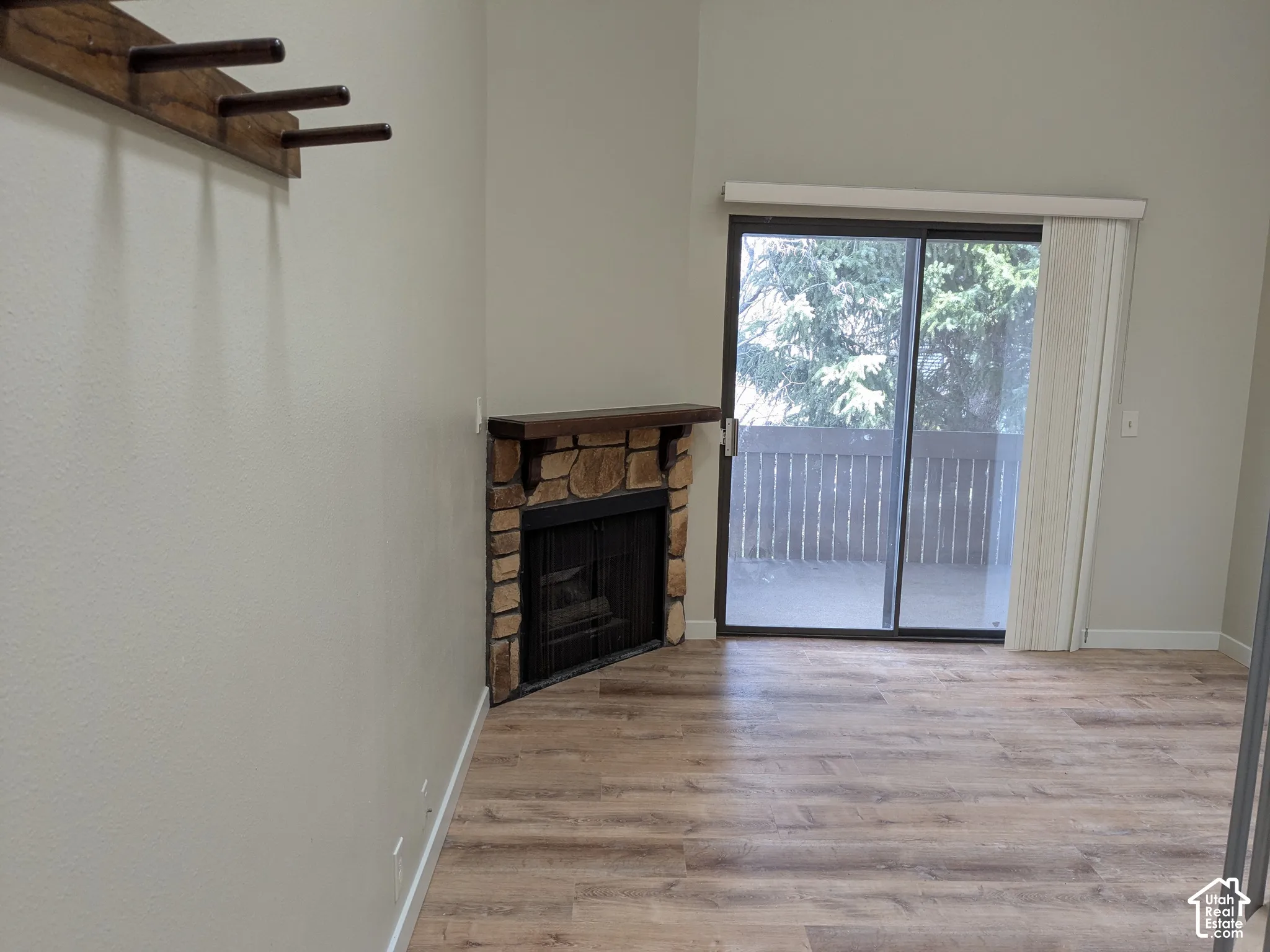 Stone-surround fireplace with a wood mantle, wood-finish flooring, and sliding glass door leading to an outdoor deck with a privacy railing