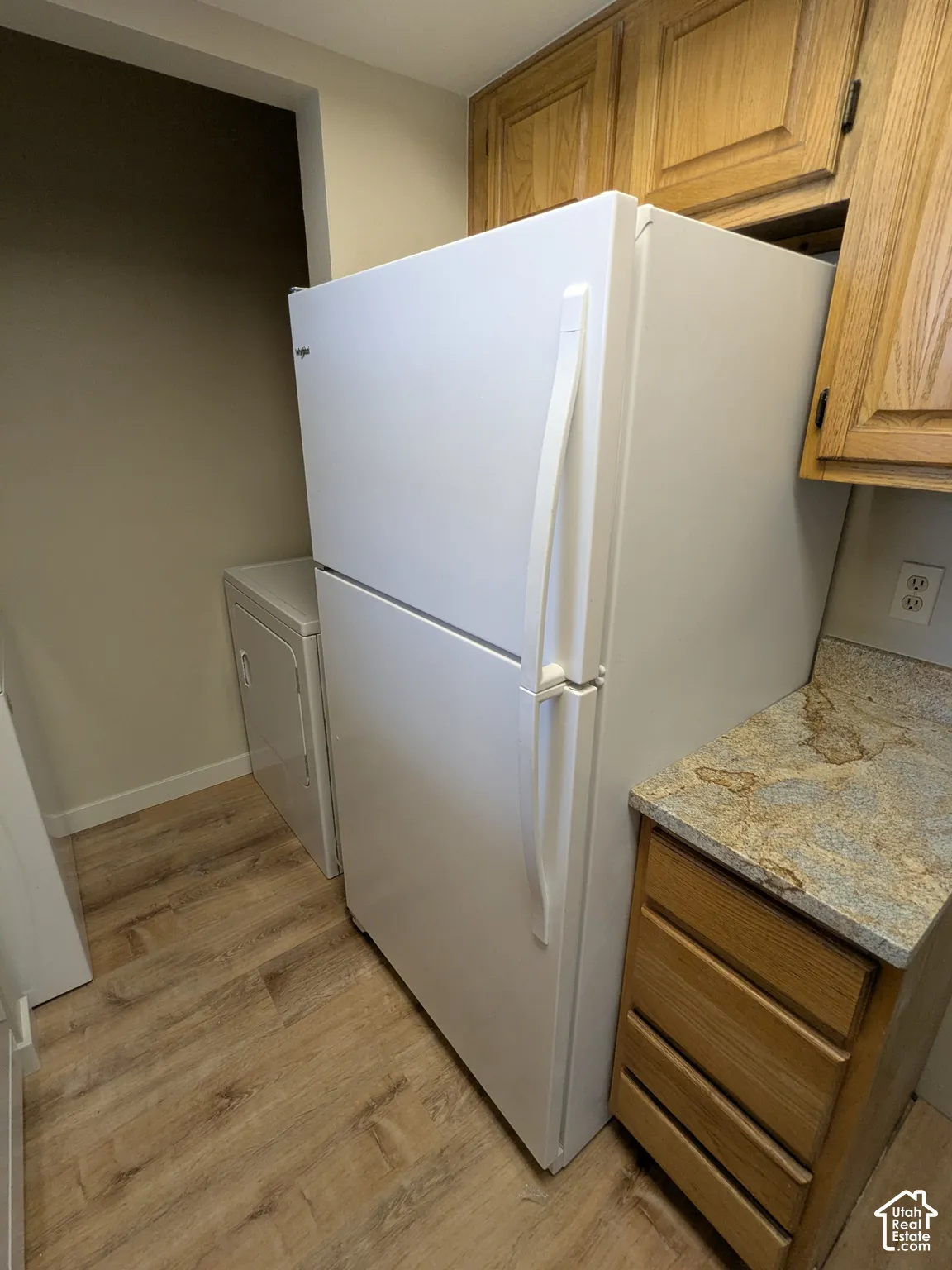 Efficient kitchen layout featuring a white refrigerator with freezer compartment, wood-finish cabinetry, and granite-style countertops