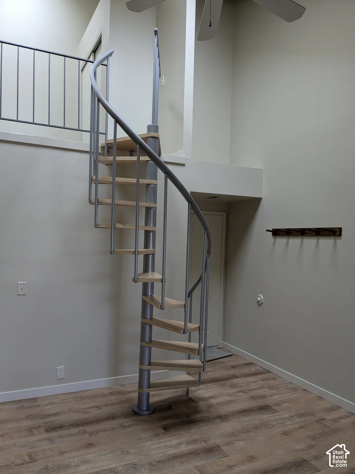 Spiral staircase with wood-finish treads and metal railing, high ceilings, wood-finish flooring, and upper-level balcony with metal railing