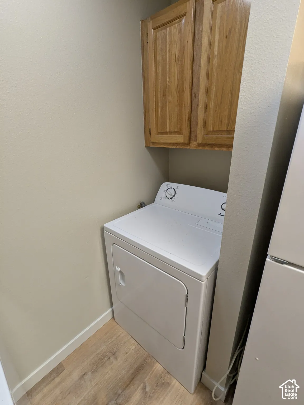 Dedicated laundry room featuring a full-size electric dryer with front-load design, wood-finish cabinetry for storage, wood-finish flooring, and ample counter space for folding and organization