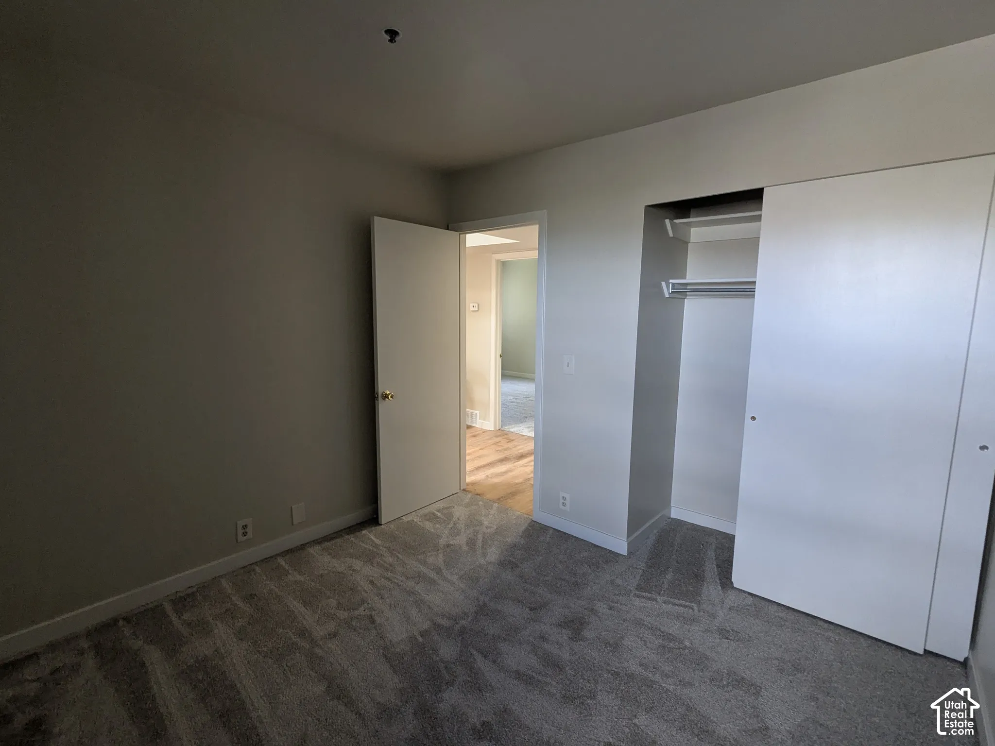Neutral tone wall paint, grey patterned carpeting, white trim, and a bi-fold closet with shelving