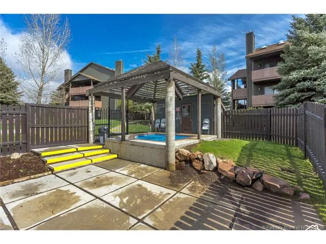 Paved patio area, stepped entry with high-visibility treads, wood privacy fencing, stone landscaping, and a covered hot tub