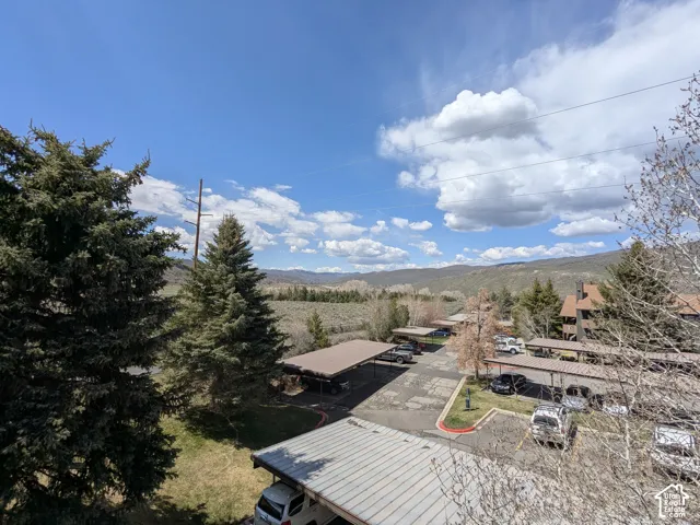 Expansive mountain landscape with mature evergreen trees, multiple covered parking structures, and a multi-level building featuring a brown exterior and pitched roofs