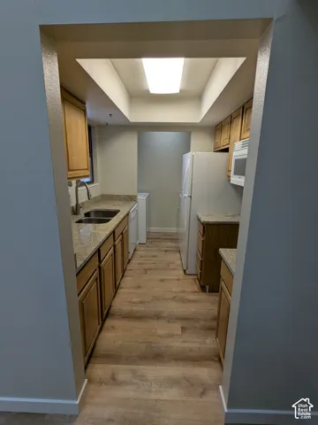 Galley kitchen featuring wood-finish flooring, wood cabinetry, stone-look countertops, a stainless steel sink, and a built-in microwave