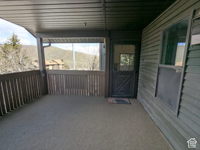 Covered outdoor patio with slatted railing, exterior siding, and a solid entry door with an upper glass pane