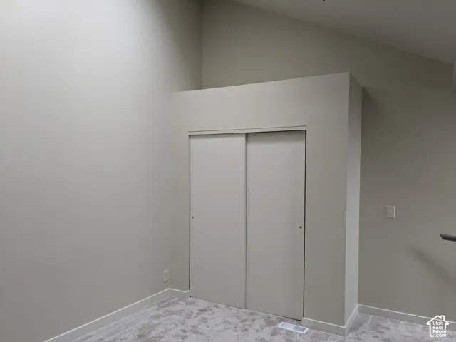 Vaulted ceiling, neutral tone walls, sliding closet doors, and light-toned carpet