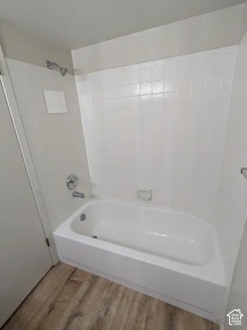 Clean, updated bathroom featuring a white subway tile surround, an alcove bathtub with chrome fixtures, and wood-finish flooring